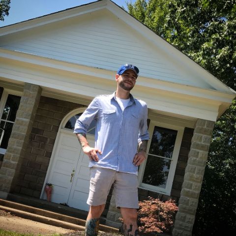 Steve Gonsalves in a blue shirt poses a picture in front of his house.